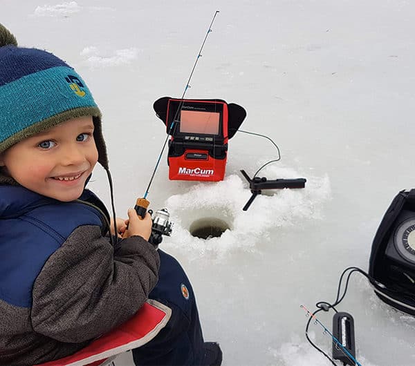 Petit garçon en train de pêcher sur la glace, une canne à pêche à la main.