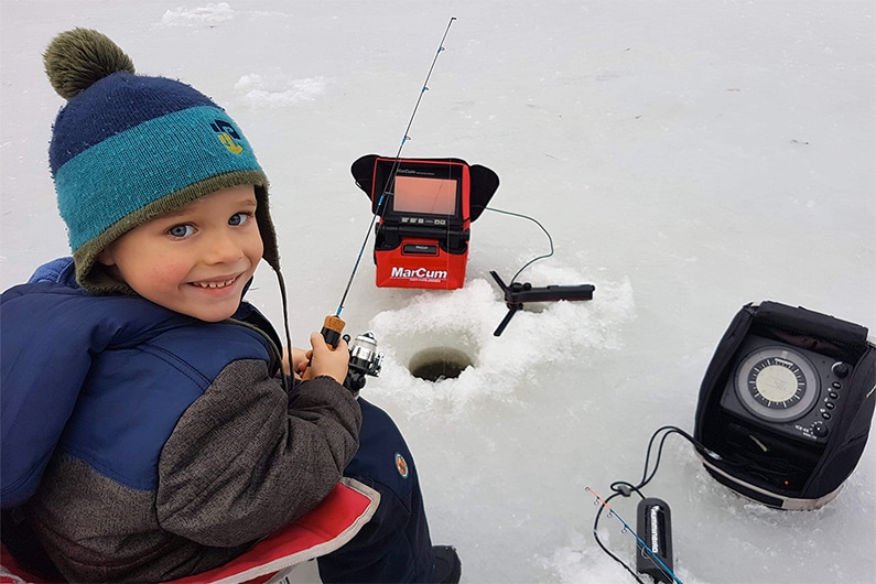 Petit garçon en train de pêcher sur la glace, une canne à pêche à la main.