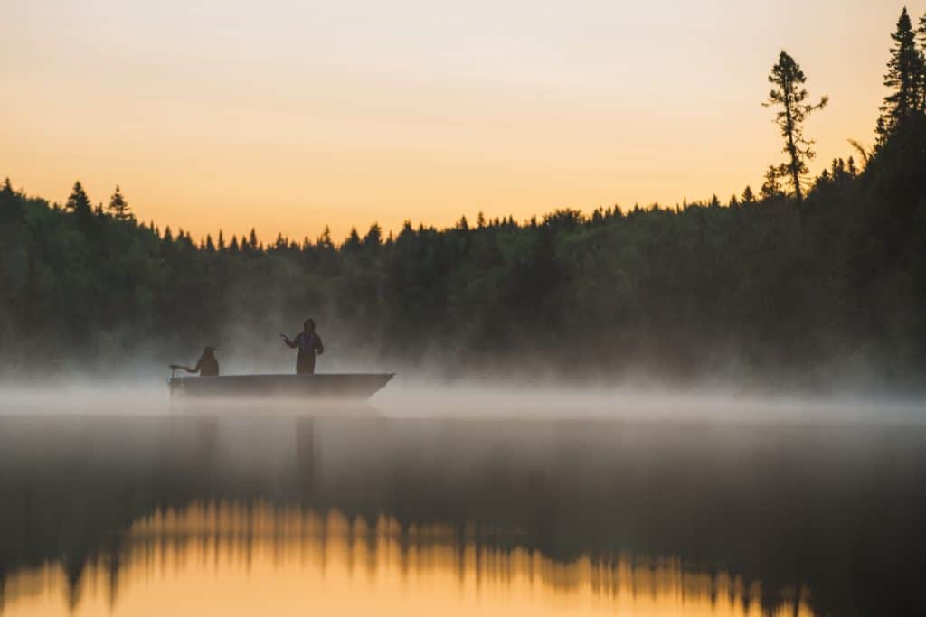 2 pêcheurs dans une embarcation lancent leur ligne au lever du soleil