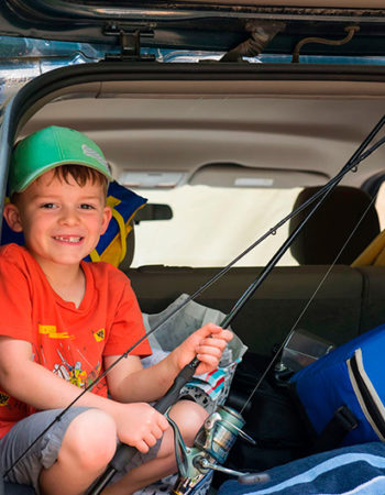 Un jeune enfant prépare sa canne à pêche bien installé dans le coffre arrière ouvert de la voiture.