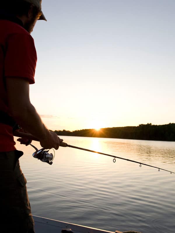 Un homme pêche debout sur un quai au crépuscule.