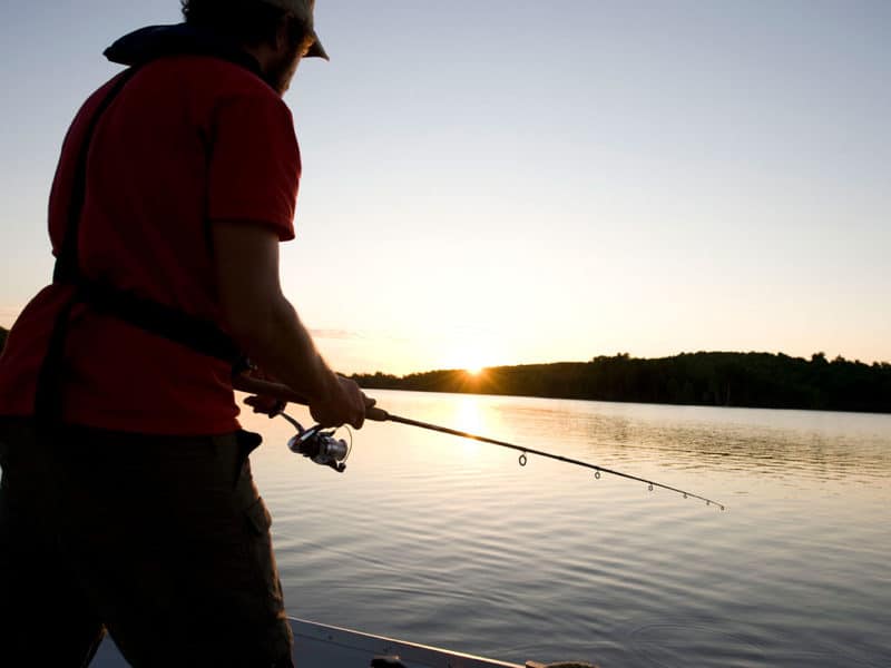 Un homme pêche debout sur un quai au crépuscule.