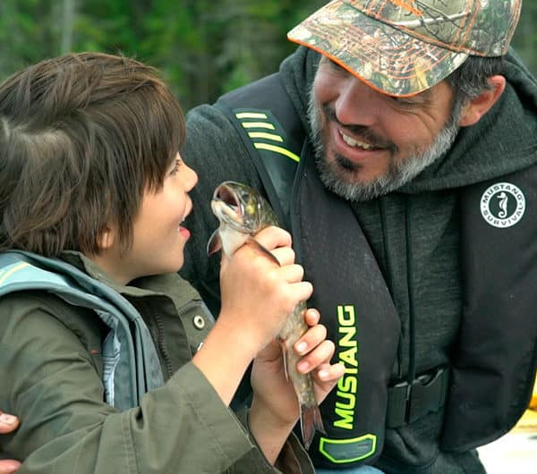 Un jeune pêcheur montre fièrement à son père la truite qu'il vient d'attraper.